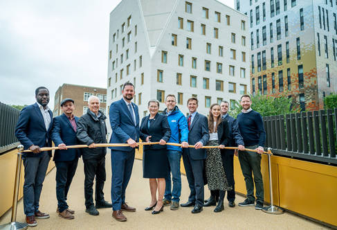 Ten people standing behind a ribbon, about to be cut, on a bridge